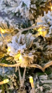 Yeşil köknar üzerine beyaz spreyli bir Noel ağacı dalı, sarı ışıklar ve kırmızı ve mavi toplarla süslenmiş bir çelenk.