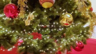 Büyük salonda kırmızı ve altın çiçeklerle süslenmiş Noel ağacı, toplar, ışıklar ve çelenkler. 