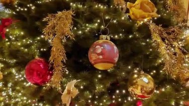Büyük salonda kırmızı ve altın çiçeklerle süslenmiş Noel ağacı, toplar, ışıklar ve çelenkler. 