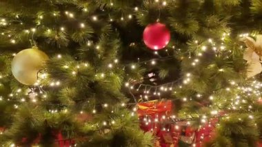 Büyük salonda kırmızı ve altın çiçeklerle süslenmiş Noel ağacı, toplar, ışıklar ve çelenkler. 