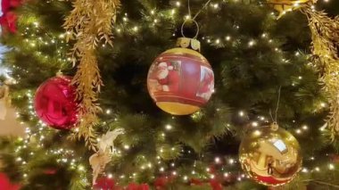 Büyük salonda kırmızı ve altın çiçeklerle süslenmiş Noel ağacı, toplar, ışıklar ve çelenkler. 