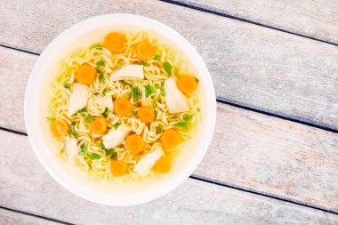 Homemade chicken soup with noodles and vegetables in a white bowl, on a  wooden background. Healthy warm comfortable food.