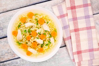 Homemade chicken soup with noodles and vegetables in a white bowl, on a  wooden background. Healthy warm comfortable food.