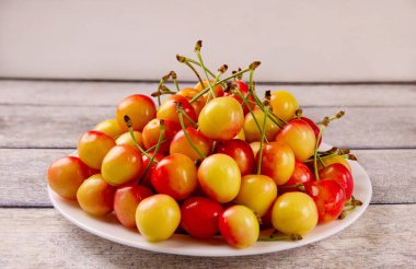 Gri ahşap arka planda yaprakları olan sarı, taze kiraz. Lezzetli kiraz