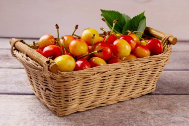 Sarı kiraz ve sepetteki yapraklar gri ahşap arka planda. Lezzetli kiraz