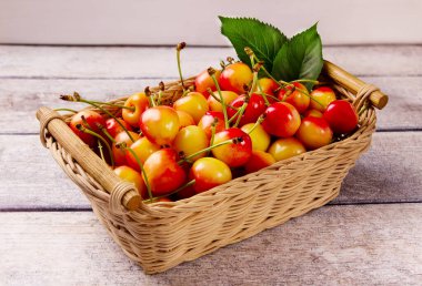 Sarı kiraz ve sepetteki yapraklar gri ahşap arka planda. Lezzetli kiraz