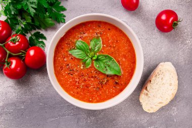 Gri arka planda fesleğen ve baharatlı ev yapımı domates kremalı çorba.