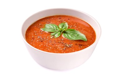 Beyaz arka planda fesleğenli ve baharatlı ev yapımı domates kremalı çorba.