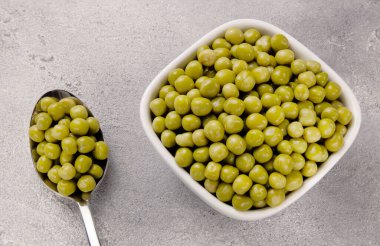 Gri arka planda bir tabakta konserve yeşil bezelye. Bezelye turşusu. Konserve yeşil bezelye.