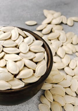 Gri arkaplanda bir kase kabak çekirdeği. Güz enerjisi yiyeceği kavramı, balkabağı, balkabağı tohumu.