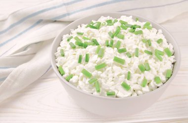 Hafif ahşap arka planda bir kasede çiftlik peyniri. Yeşil soğanlı süzme peynir. Kasedeki süzme peynir..