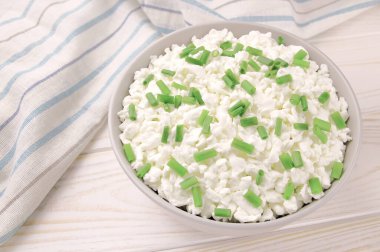 Hafif ahşap arka planda bir kasede çiftlik peyniri. Yeşil soğanlı süzme peynir. Kasedeki süzme peynir..