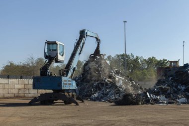 Büyük kazıcılar geri dönüşüm için hurda metaller üzerinde çalışıyor, güneşli bir gün..