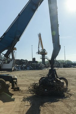 Büyük kazıcılar geri dönüşüm için hurda metaller üzerinde çalışıyor, güneşli bir gün..