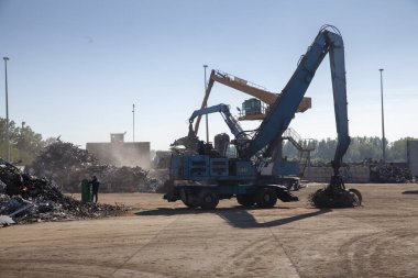 Büyük kazıcılar geri dönüşüm için hurda metaller üzerinde çalışıyor, güneşli bir gün..