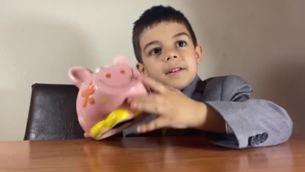 Gyerekmegtakarítás Egy Óvodás Fiú Üzleti Öltönyben Aki Egy Malacperselyt Forgat — Stock videók
