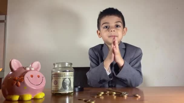 貪欲な子供のビジネスマンだ 彼の家の鍵をテーブルの上に貯金箱やコイン 貯金箱を持つ未就学児 不動産投資の概念 高品質4K映像 — ストック動画