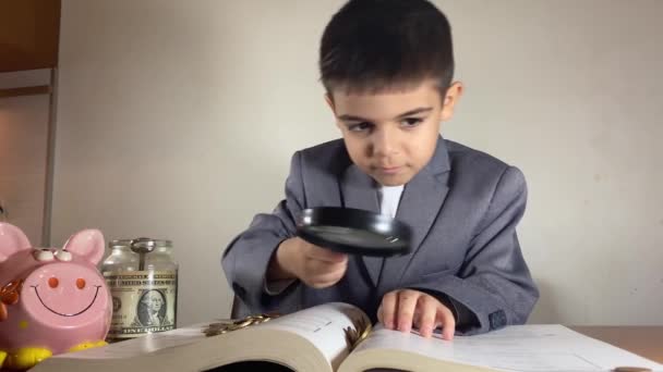 穿着智能西装的男孩拿着放大镜翻阅着这本书 找到了钱 投资于教育概念 高质量的4K镜头 — 图库视频影像