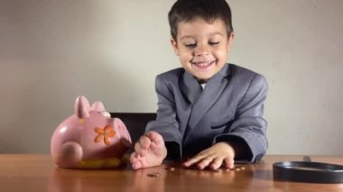 Küstah açgözlü anaokulu çocuğu, takım elbiseli çocuk domuz kumbarasından paraları sayıyor. Yatırım konsepti ve çocuk tasarrufu. Yüksek kalite 4k görüntü