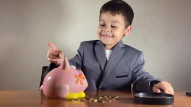 Şirin çocuk, takım elbiseli çocuk para sayıyor ve kumbarayı dolduruyor. Çocuk gelecek için para biriktiriyor. Yüksek kalite 4k görüntü