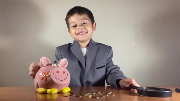 虫眼鏡で貯金箱を調べるスーツの子供 投資前の調査とデューデリジェンス 高品質4K映像 — ストック動画