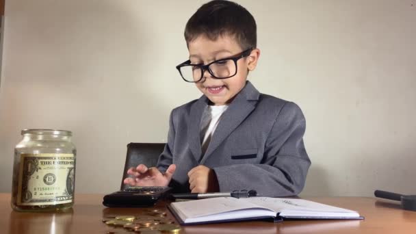 带着眼镜可爱的孩子 适合算计利润 并在罐子里装满了节约的钱 用计算器写在杂志上财务计划的概念 高质量的4K镜头 — 图库视频影像