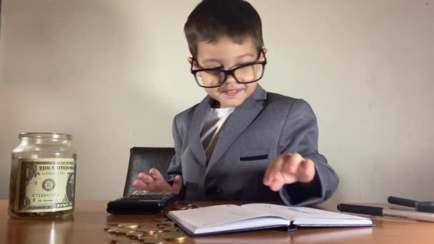 带着眼镜可爱的孩子 适合算计利润 并在罐子里装满了节约的钱 用计算器写在杂志上好奇的兄弟走进镜框 高质量的4K镜头 — 图库视频影像