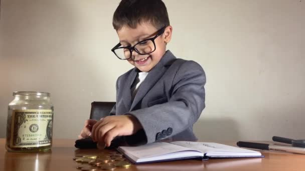 带着眼镜的可爱孩子 适合数钱 并把钱装进装有储蓄的罐子 用计算器写在杂志上 是的高质量的4K镜头 — 图库视频影像