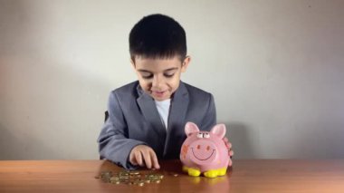 İçine para koyduktan sonra kumbarasını öpen takım elbiseli şirin bir çocuk. Erken yaştan biriktirdiğim paralar. Yüksek kalite 4k görüntü