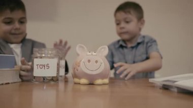 Finansal eğitim. İstek ve ihtiyaçlar. Çocuklar oyuncak kavanozundan acil durum tasarruf kavanozuna para transfer ediyorlar. Ağır çekim. Yüksek kalite 4k görüntü
