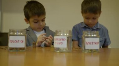 Takım elbiseli çocuk sikkeleri karıncaya benzetiyor ve değer başına istifliyor. Kardeşi para kavanozlarına yardım ediyor. Seçici odaklanma. Yüksek kalite 4k görüntü