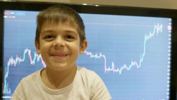 早期投资 金融教育 学龄前男孩笑着在股市图表前摇动着 在储蓄罐上打盹 高质量的4K镜头 — 图库视频影像