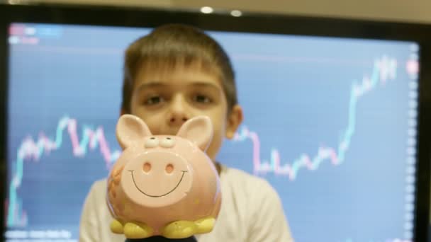 初期投資 金融教育について 子供の貯金 ボーイは 株式市場のチャートの前で彼の豚肉銀行を抱きしめました 高品質の4K映像 — ストック動画