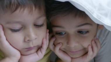 Soğuk kış gününde yorganla kaplı iki çocuk yatakta çizgi film izliyor. Ağır çekimde yüz ifadeleriyle kapatın. Yüksek kalite 4k görüntü
