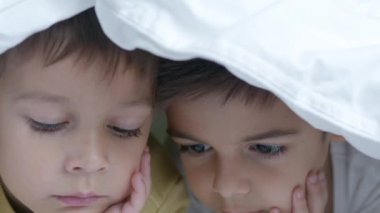 Soğuk kış gününde yorganla kaplı iki çocuk yatakta çizgi film izliyor. Ağır çekimde yüz ifadeleriyle kapatın. Yüksek kalite 4k görüntü