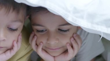 Soğuk kış gününde yorganla kaplı iki çocuk yatakta çizgi film izliyor. Ağır çekimde yüz ifadeleriyle kapatın. Yüksek kalite 4k görüntü