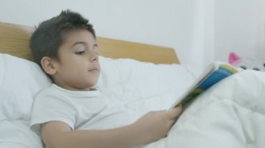 Tatlı çocuk, yatakta kitap okuyan çocuk. Orta yavaş çekim. Yüksek kalite 4k görüntü