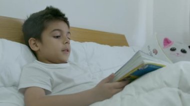 Tatlı çocuk, yatakta kitap okuyan çocuk. Orta yavaş çekim. Yüksek kalite 4k görüntü