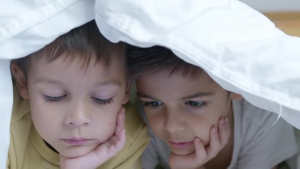 在寒冷的冬日 两个孩子躺在床上看卡通片 上面盖着被子 用面部表情紧闭慢动作 高质量的4K镜头 — 图库视频影像