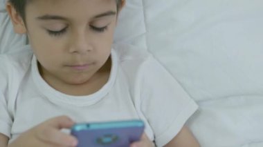Tatlı beyaz çocuk yatakta uzanıyor ve telefonda çizgi film seyrediyor. Yüksek kalite 4k görüntü