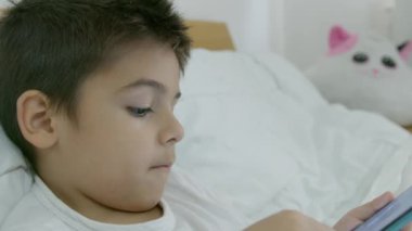 Tatlı beyaz çocuk yatakta uzanıyor ve telefonda çizgi film seyrediyor. Yüksek kalite 4k görüntü