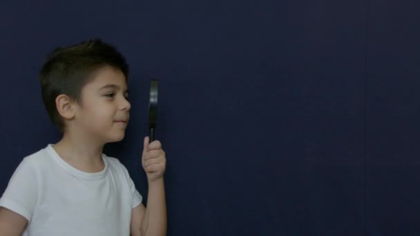 男孩透过放大镜 在蓝色的背景上左右为难地走着 慢动作高质量的4K镜头 — 图库视频影像