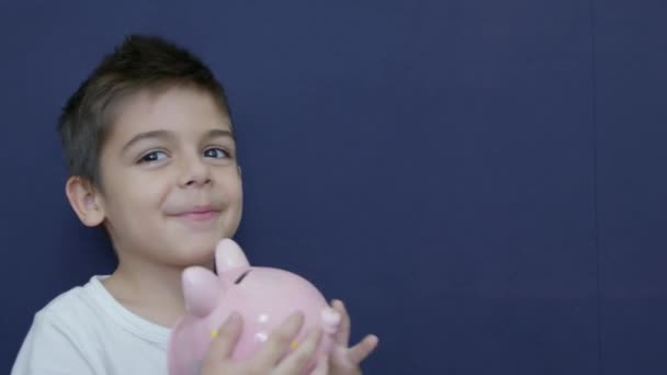 Gyerekmegtakarítási Koncepció Kaukázusi Fiú Aki Vicces Arckifejezésekkel Ölelgeti Malacperselyét Kék — Stock videók