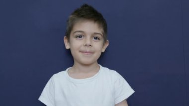 Kafkasyalı çocuk elini alnına koydu. Şaşırmış, şok olmuş, sinirli bir yüz ifadesi. İnanmıyorum. Mavi arka planda yavaş çekim izole edildi. Yüksek kalite 4k görüntü
