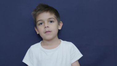 Huysuz, yüzü ve çocuğu stüdyoda. Sinirli çocuk mavi arka planda izole edilmiş. Duygular, yüz ifadesi, ağır çekim. Yüksek kalite 4k görüntü