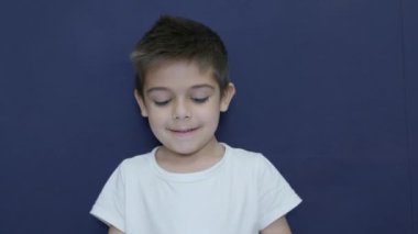 Sevimli küçük çocuk baş parmağını kaldırıyor, mutlu yüz ifadesi, duygu, mavi arka planda yavaş çekim. Yüksek kalite 4k görüntü