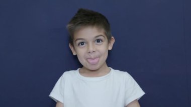 Küçük beyaz çocuk mavi arka planda izole bir şekilde yavaş çekimde dil ve dans gösteriyor. Yüksek kalite 4k görüntü
