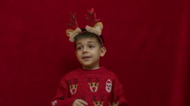 Noel 'de ren geyiği boynuzları takan anaokulu çocuğu. Çirkin süveteri olan, bir şeyleri açıklayan ve baş parmağını kaldıran. Ağır çekim. Yüksek kalite 4k görüntü