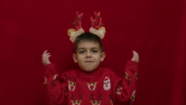 わからないわ クリスマスの醜いセーターとトナカイの耳と角でかわいい子供の無力な手のジェスチャー 何のアイデアもなく 不確実性を感じるのです 高品質の4K映像 — ストック動画