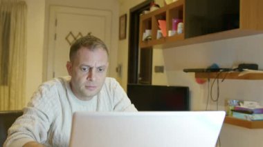 Evde dizüstü bilgisayar kullanan orta yaşlı beyaz bir adam. Uzaktan çalışma konsepti. Yüksek kalite 4k görüntü